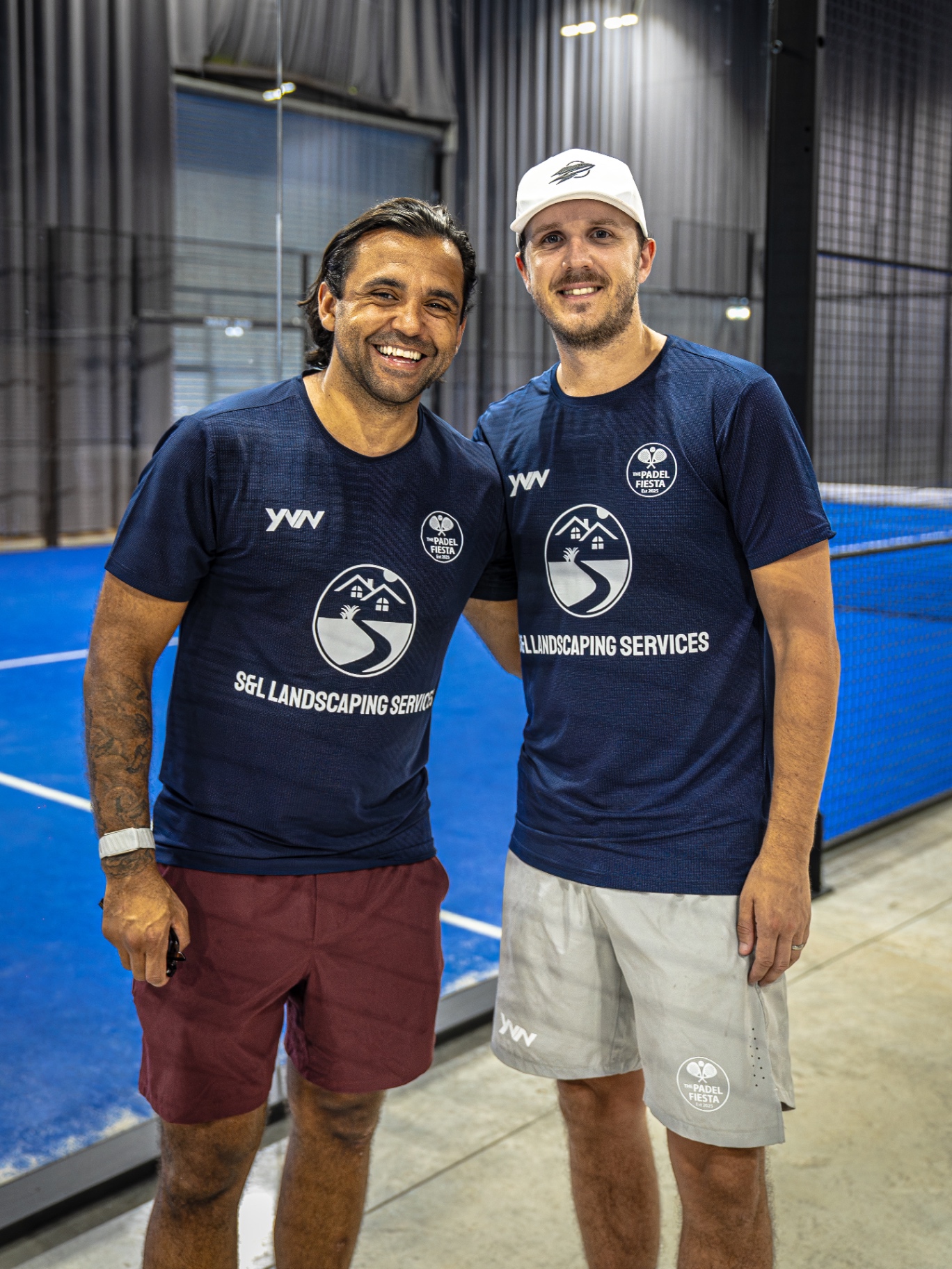 The Padel Fiesta cofounders in branded navy t-shirts on a blue padel court