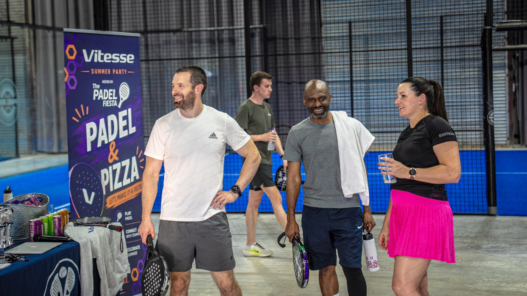 Corporate guests chatting courtside beside a Padel & Pizza event banner