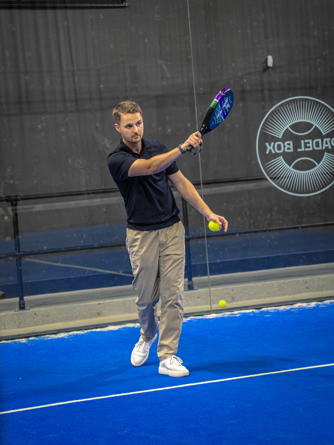 Player serving with a forehand swing on an indoor padel court