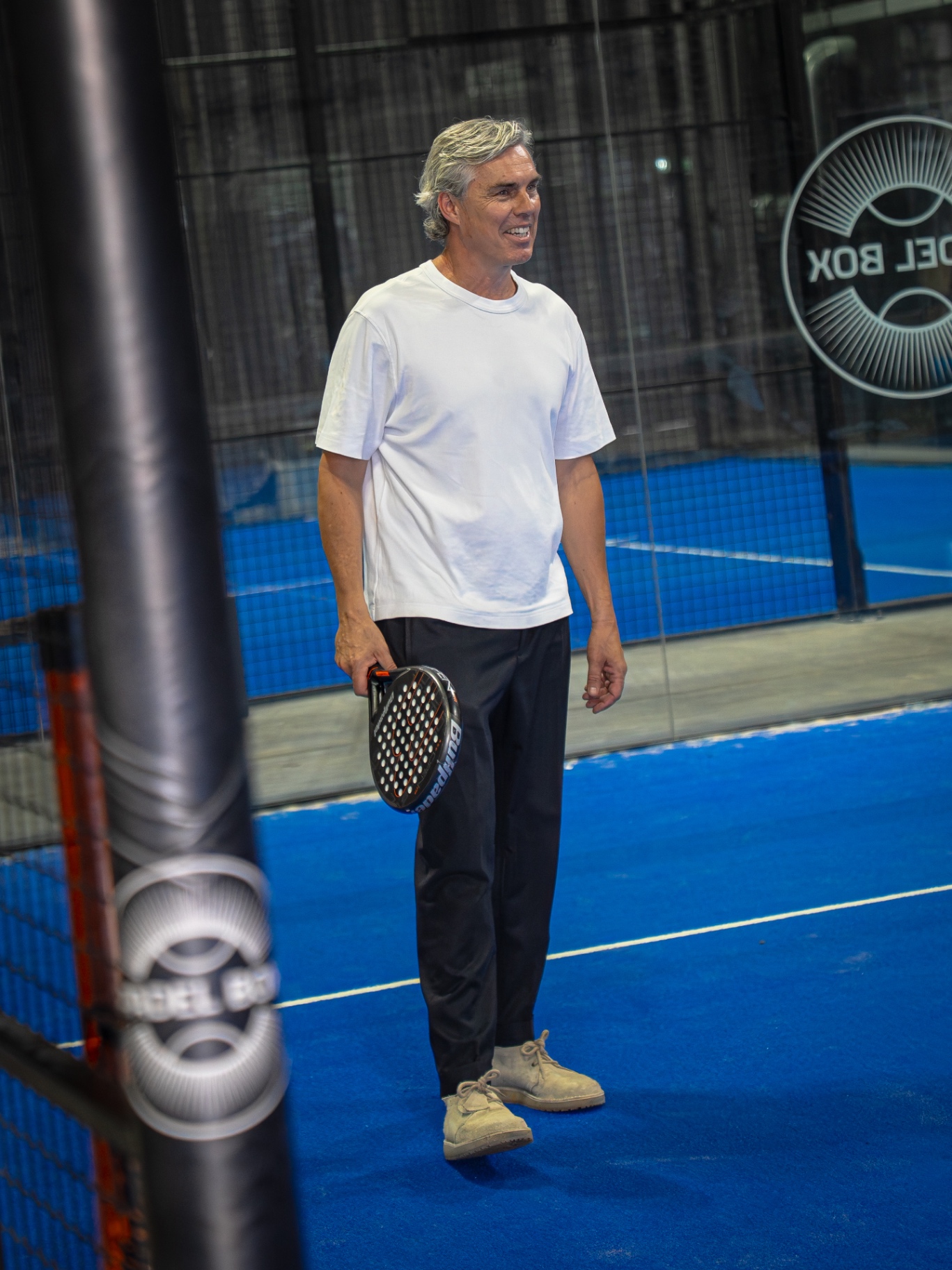 Guest smiling courtside holding a padel racket between games